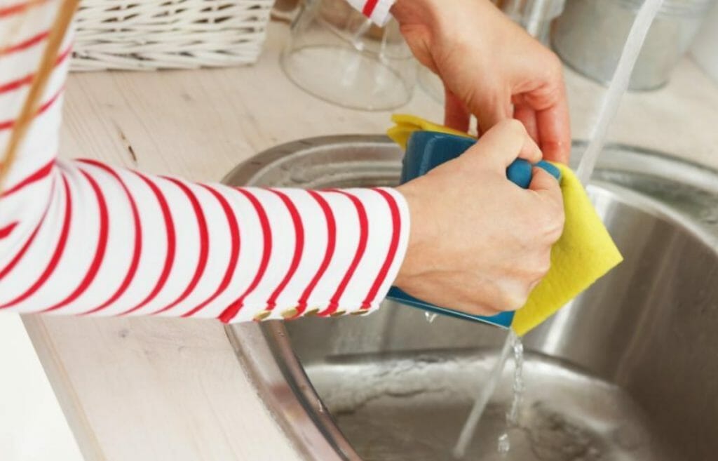 Close up shot of hands using a sponge in the kitchen sink