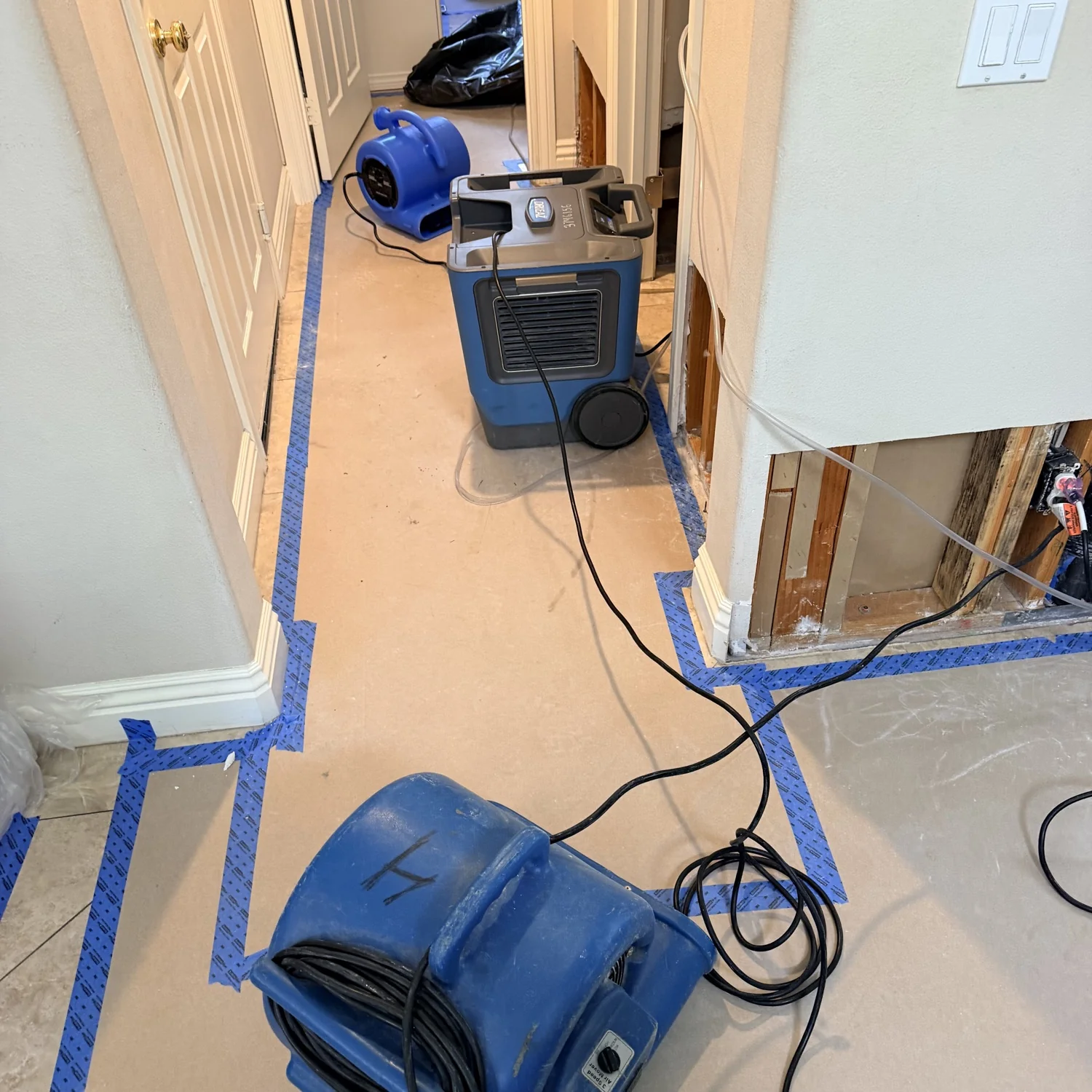 Air movers and dehumidifier drying a hallway after a pipe leak