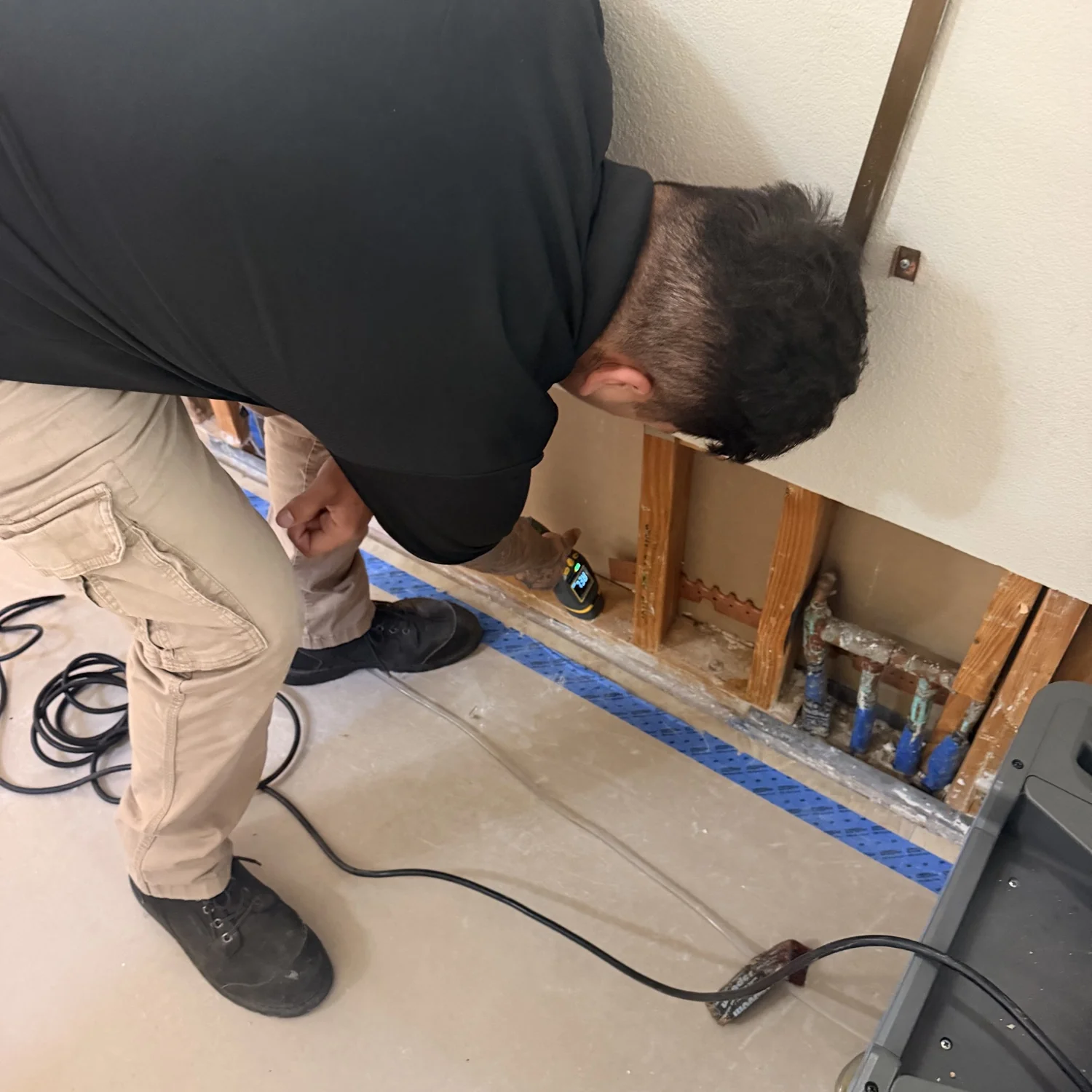 Flood Brothers plumber checking pipes behind a drywall cutout during leak detection