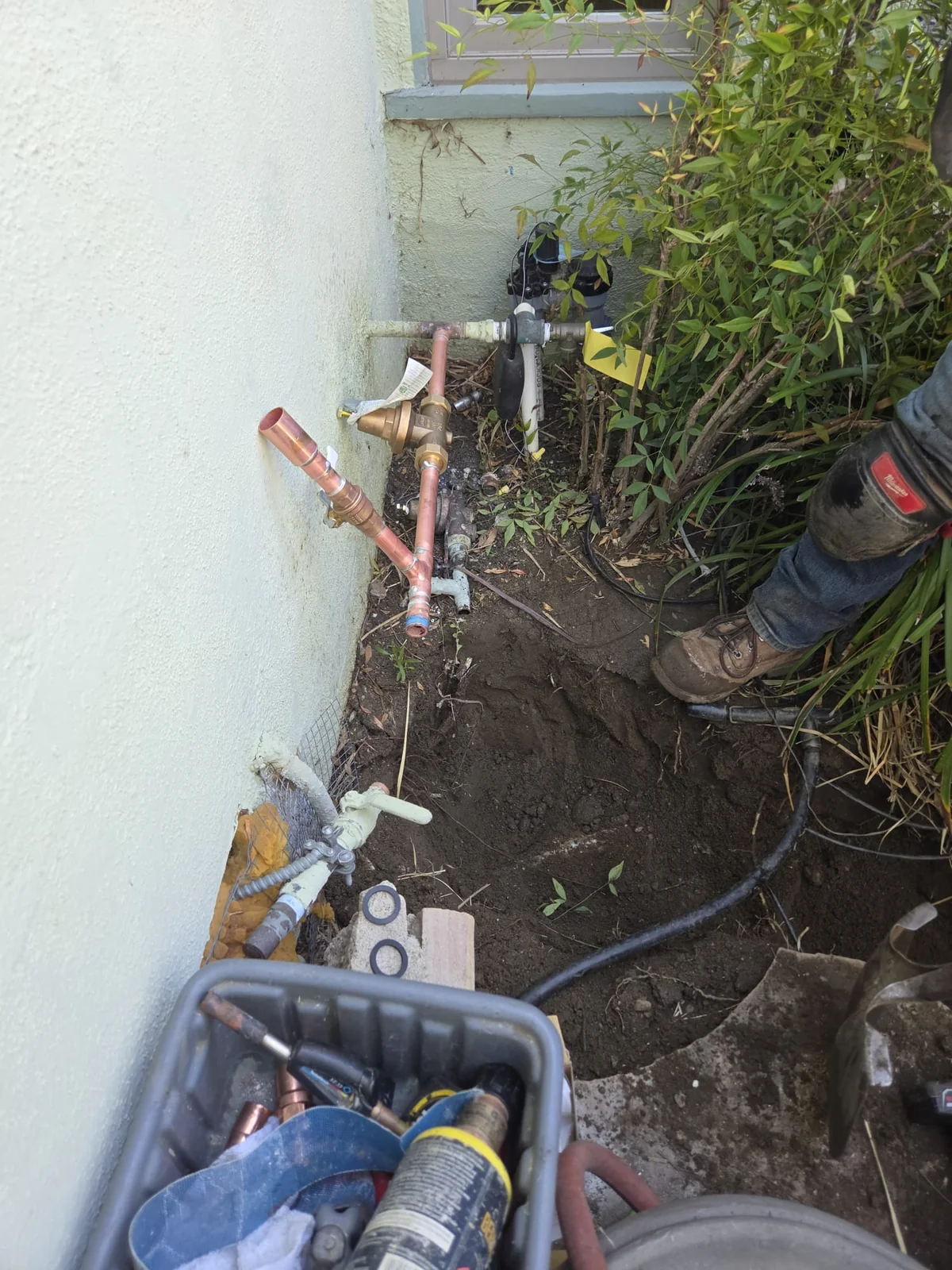 Flood Brothers plumber fitting a new main shutoff valve on copper water line beside a house